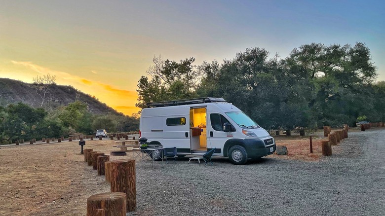 Camper van parked at a campsite in Caspers Wilderness Park at sunset, surrounded by oak trees, picnic tables, and wooded hills