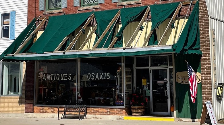 The front of Antiques Osakis with a tattered green awning, glass windows and American flag.