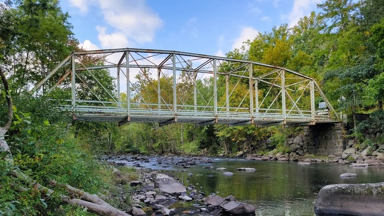 Views of a steel bridge spanning a rocky creek at Green Lane Park in Pennsylvania, surrouned by trees.