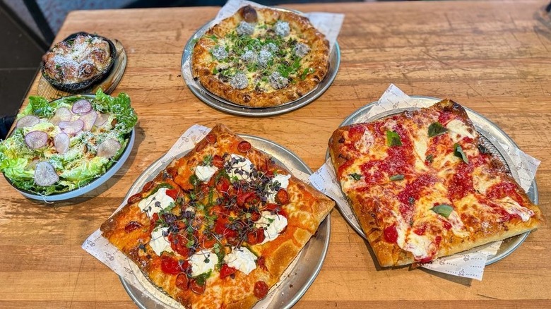 Truly Pizza's square and round pies on a wooden table at its Dana Point location