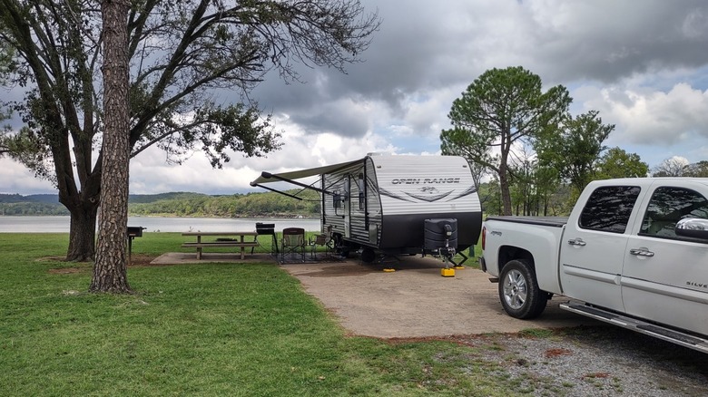 A camping trailer with an awning parked as a grassy campsite shaded by trees and overlooking a lake at Cherokee Landing State Park.