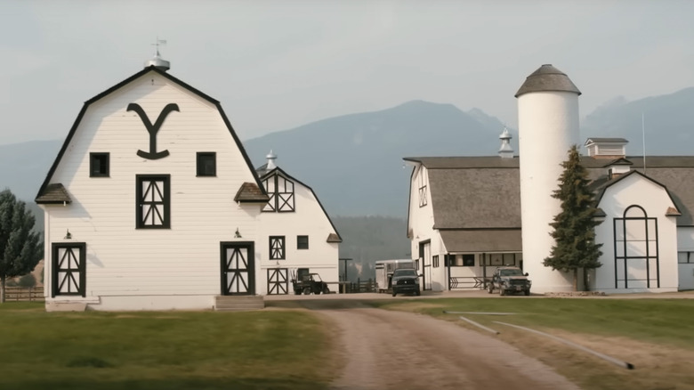 Exterior of white barns from "Yellowstone" with mountains behind them.