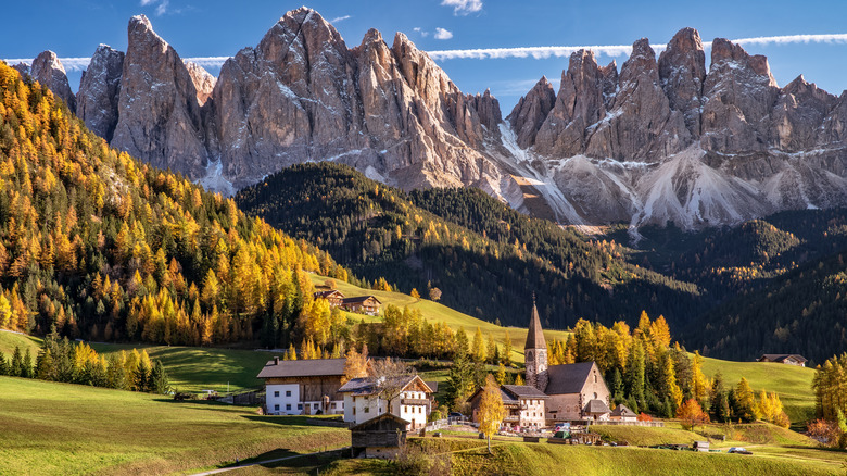 View of Val di Funes with mountains, meadows, valleys, and a church in the foreground during the day.