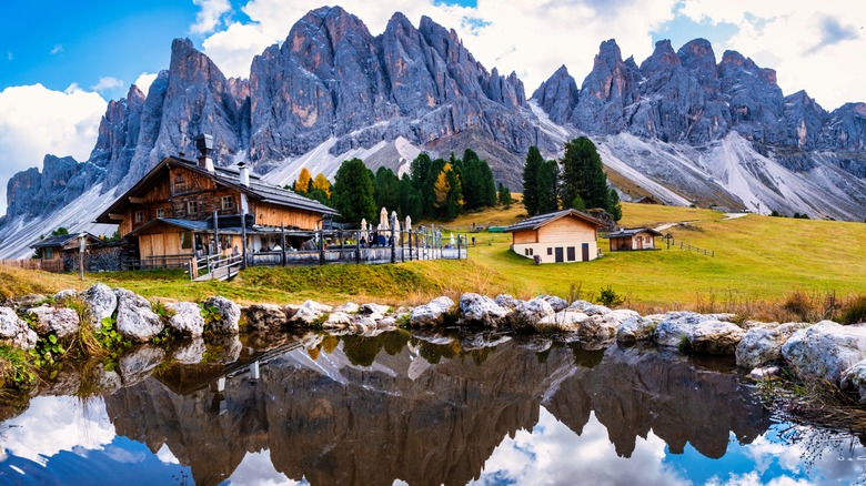 View of Geisleralm, a small alpine hut with mountains and a pond surrounding in Val Di Funes, Italy.