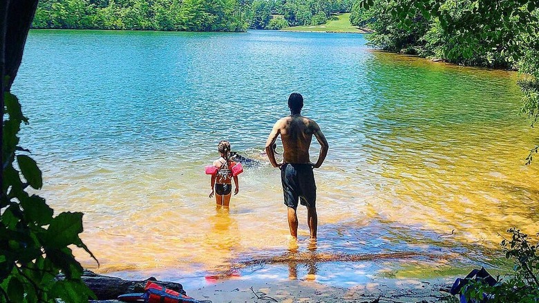 A man and girl with arm swim floats looking at a lake