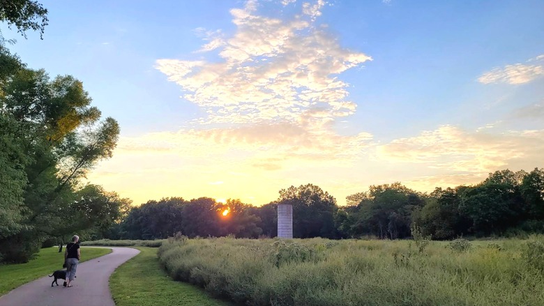 person walking a dog on a trail surrounded by greenery, Lake Springfield Park and Boathouse, Missouri