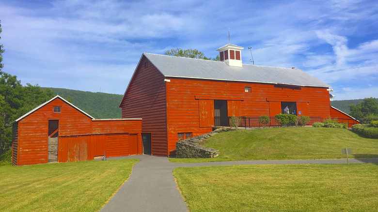 A red barn structure known as the Blenheim-Gilboa Visitors Center, pictured during the day with mountains and trees in the background.