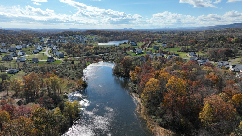 A river framed by autumn trees in a valley with a small town visible in the back