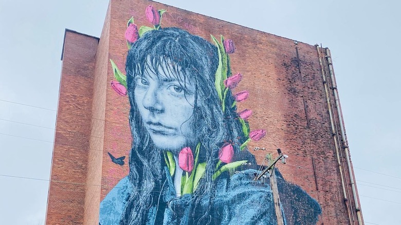 Giant mural on side of brick building depicting a young woman with pink tulips in her hair