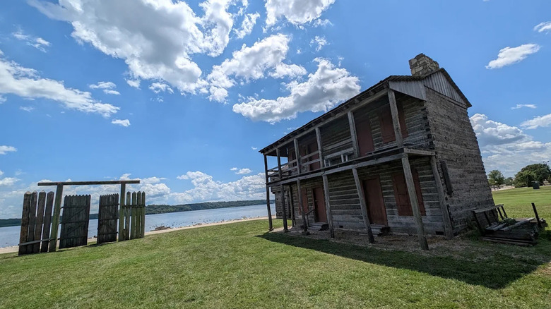 A portion of the recreated, wood-and-brick Fort Madison directly beside the Mississippi River with green grass and partly cloudy skies