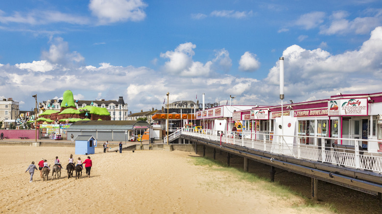 Tourists ride ponies past a row of beachside businesses on a sunny day in Great Yarmouth, UK