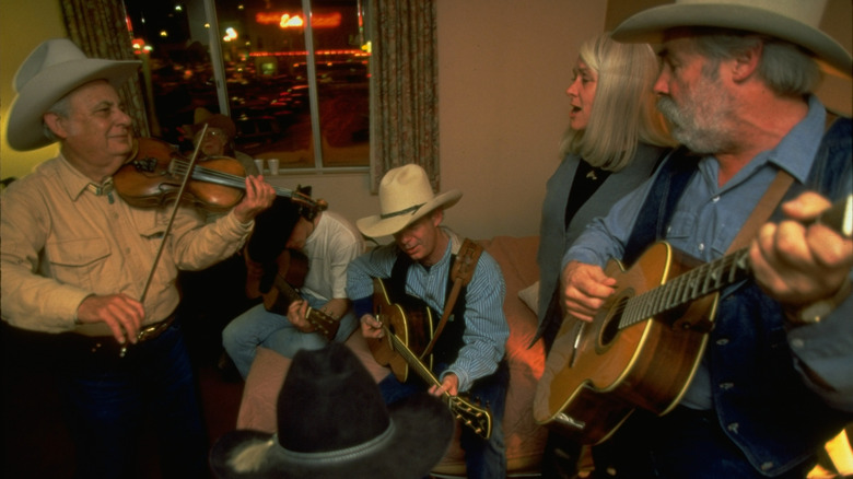 Cowboys and cowgirls gathered around playing a violin and guitars.