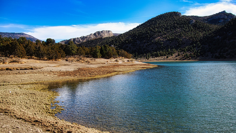 Green mountains blue sky behind still lake