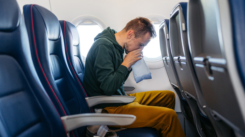 Distressed young man vomiting in a sick bag in an airplane