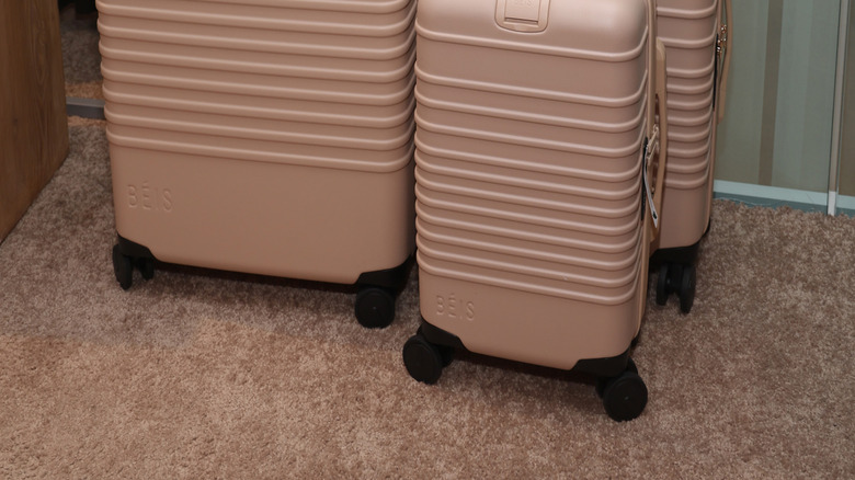 Pink Beis suitcases standing next to each other on plush carpet.