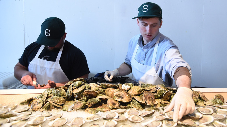 Two men shucking and serving oysters at an oyster festival.