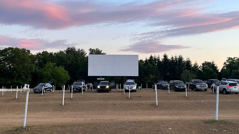 View of cars parked in front of a drive-in movie screen at sunset.