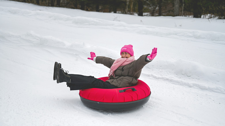 A woman happily snow tubing down a hill in winter