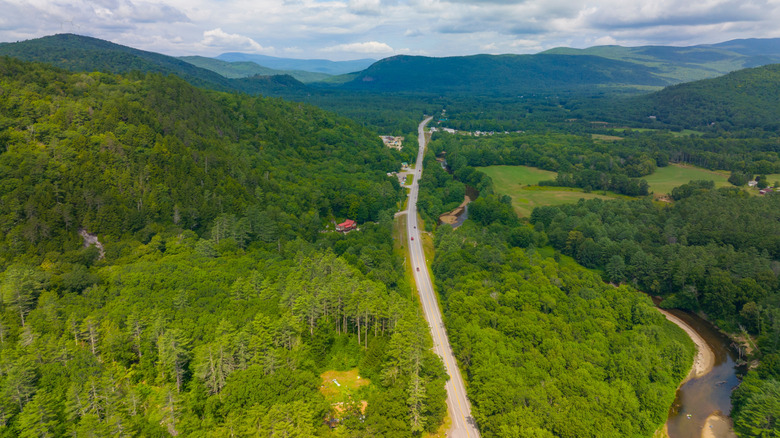An aerial shot of a road cutting through green forest into the White Mountains of New Hampshire
