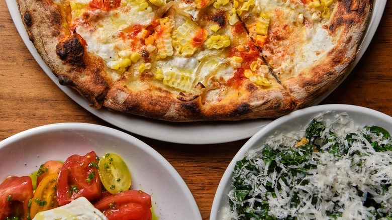 Typical Italian food: artisanal pizza topped with tomato sauce, mozzarella, and corn, cherry tomatoes and mozzarella, and roasted green peppers topped with grated cheese