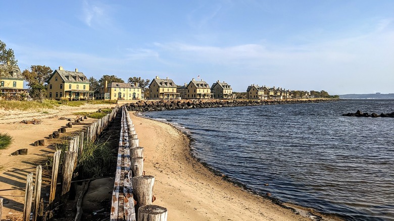Sandy shore with a wooden fence and rock seawall on the left and blue water on the right
