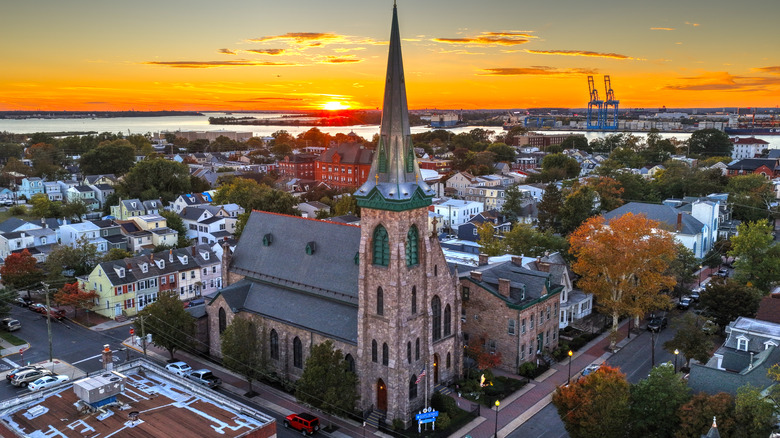 Aerial view of Gloucester City's streets and houses with a towering church steeple and the nearby Delaware River with Philly shipping ports on the opposite side