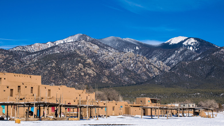Some buildings in Taos Pueblo in front of a backdrop of snow-covered mountains