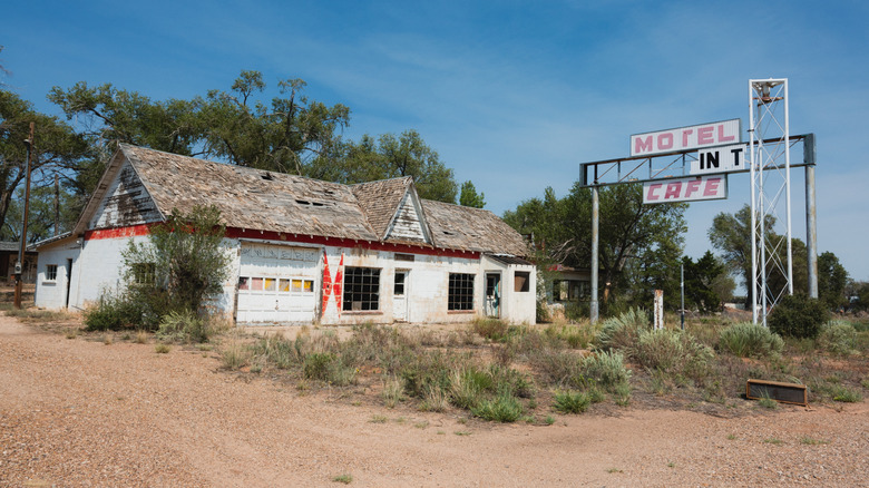 Abandoned motel in Glenrio, a white dilapidated building with a sign out front and trees in the background, under a blue sky