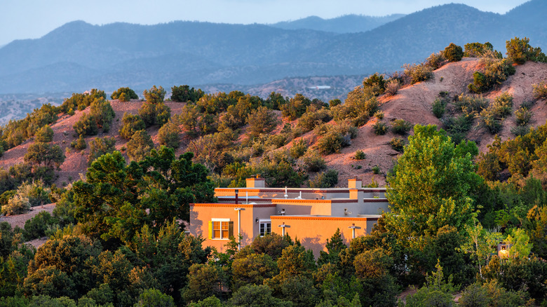 Single house in the Tesuque community with desert, trees, and mountains in the background during sunset.