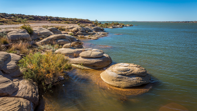Smooth boulders line the shoreline of Ute Lake in New Mexico on a blue-sky day.