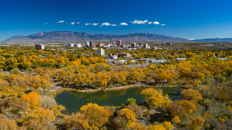 Panoramic view of Paradise Hills, Albuquerque, with autumn trees and a small lake in the foreground, and mountains in the background