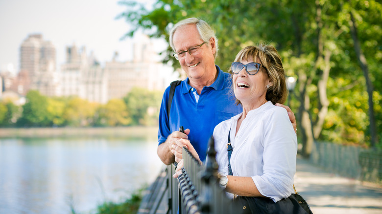 A smiliing senior couple leaning against a park rail in Central Park, New York City