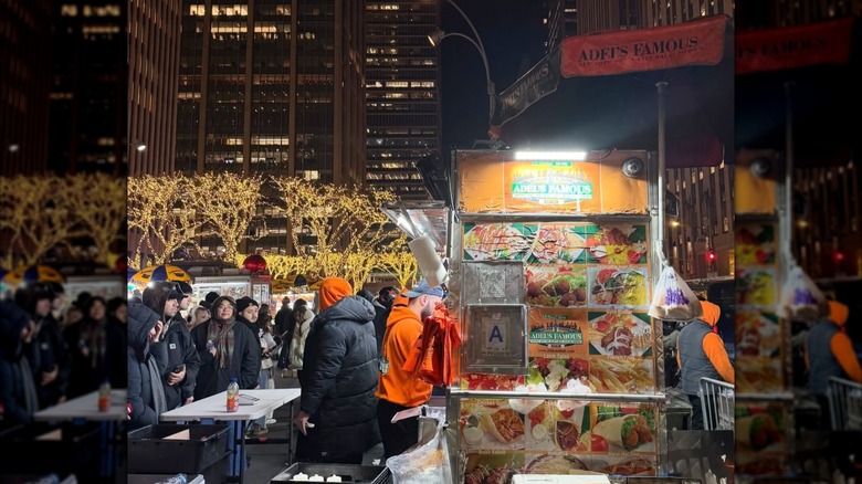 People gathered next to Adel's Famous Halal Food cart in NYC at night