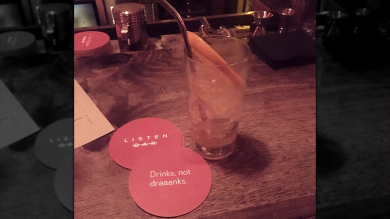 A cocktail glass with a straw next to Listen Bar coasters