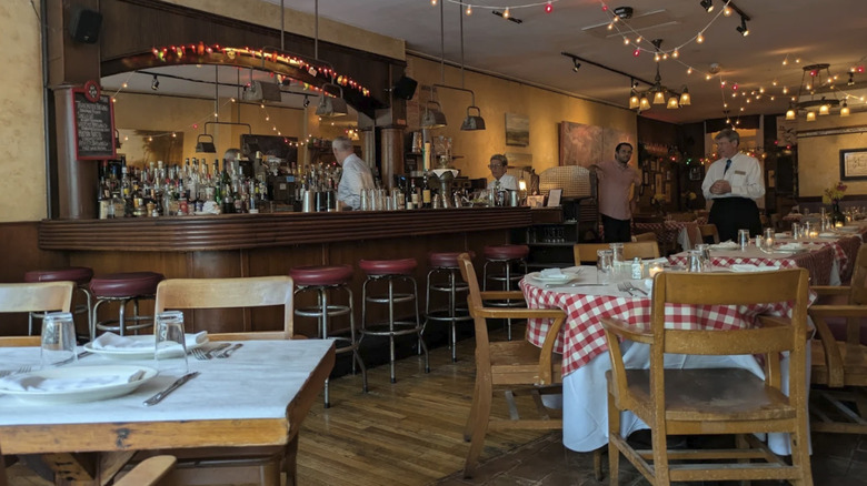 A view of the interior of Noodle Pudding, showing tables with red-checkered tablecloths and a large bar.