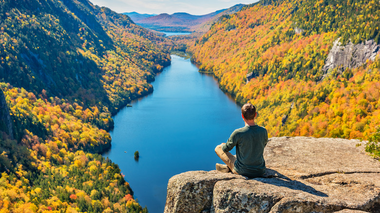A hiker sitting on a rock looking out across a river in the Adirondack Mountains, NY