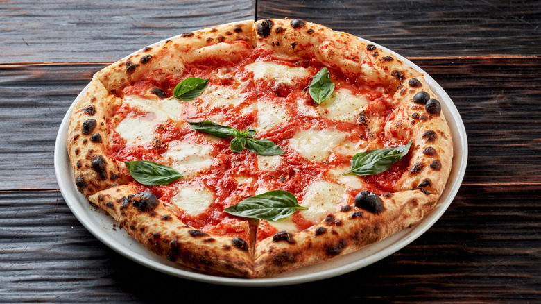 Neapolitan Margherita pizza with melting mozzarella, tomato sauce, and basil leaves on a dark wooden background