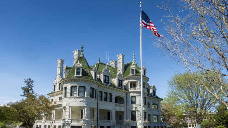 Stone estate with a green tiled roof and ornate turrets, set on a lush lawn under a clear blue sky with a star and stripes flag, Webb Horton Mansion, Middletown