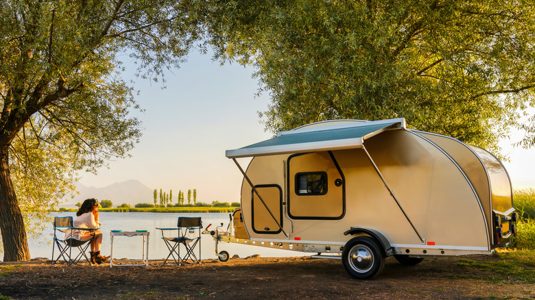 Woman enjoying lakeside campsite views with a small camper