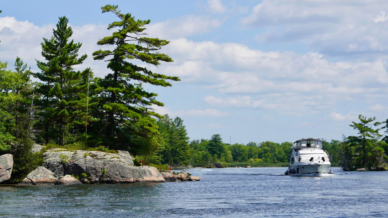 A boat moves past the rocky shore on Lake Ontario on a sunny day.