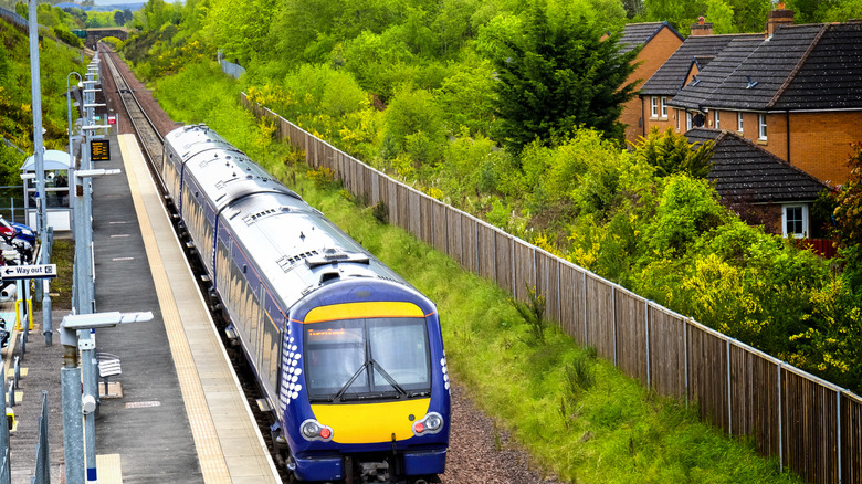 A train puling into a station with a fence and a few houses to the side in Newtongrange in Scotland