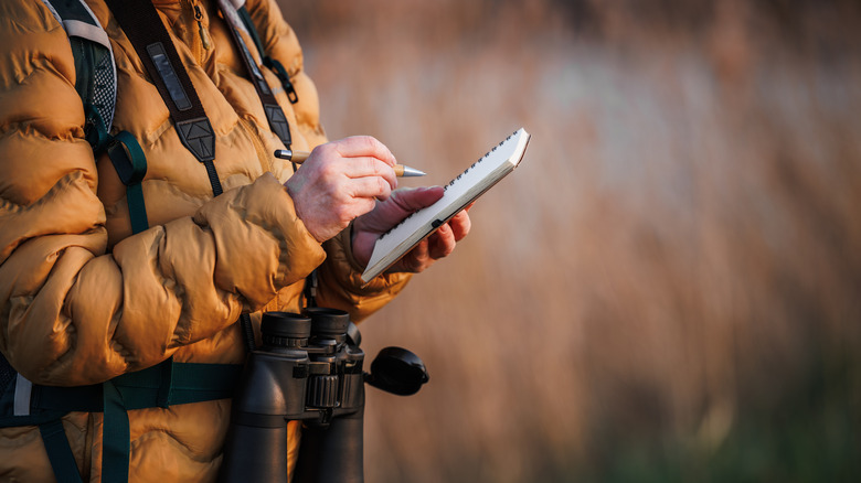 A birder in a winter jacket checks a bird of a checklist.