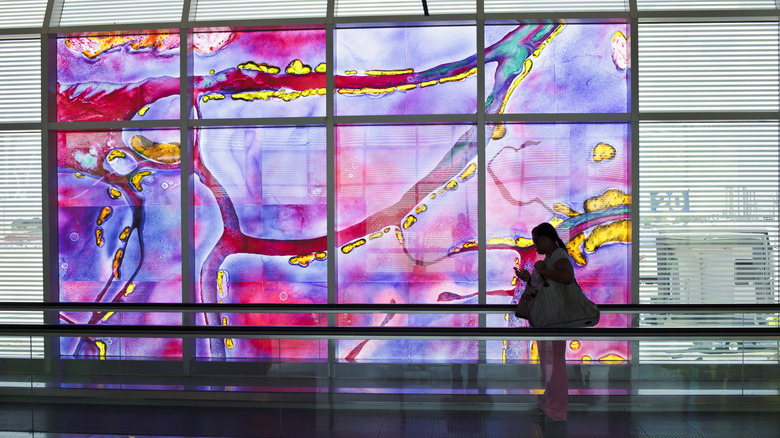 A woman rides a moving walkway past a colorful digital mural at a Houston airport