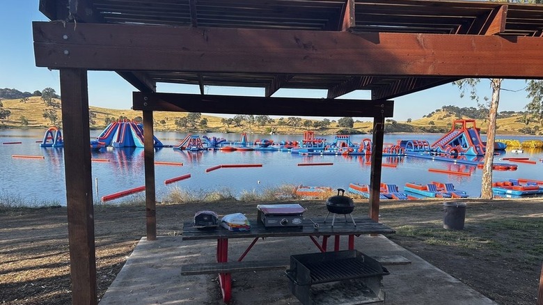A shaded picnic table at Splash-n-Dash Aqua Park, with inflatables on the water in the background