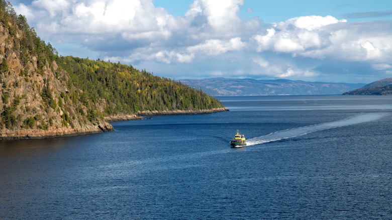 A boat sailing along the Saguenay Fjord next to towering cliffs in Quebec, Canada