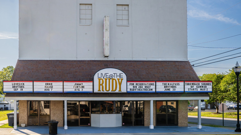 The exterior facade of Rudy Theatre with signs for upcoming shows and glass-door entries.