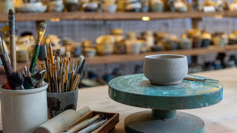 Pottery bowl on wheel, paintbrushes, pots on shelves
