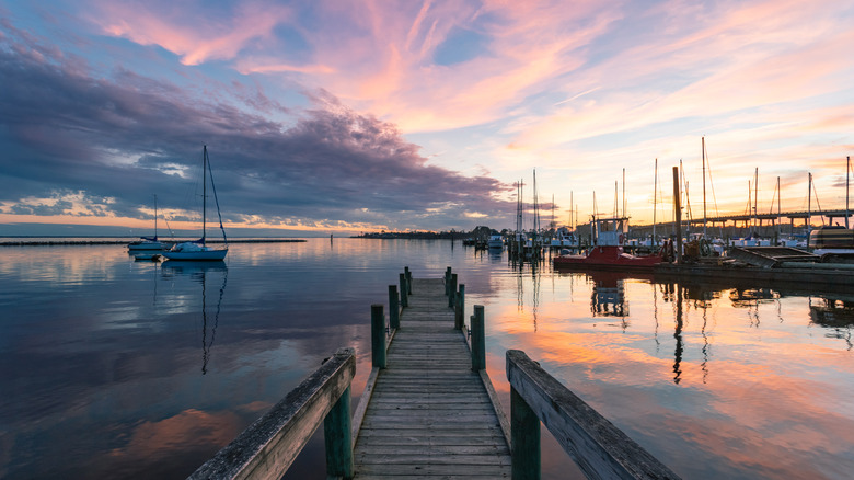 Sun setting over the water and marina filled with sailboats in Oriental, viewed from a small timber pier.