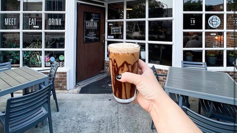 A woman holding a coffee in front of Carolina Coffee Shop