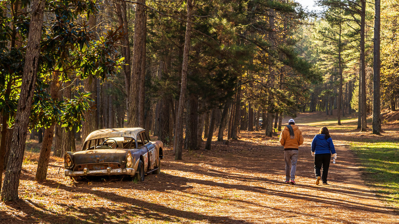 Two hikers walk down a peaceful path next to a vintage car on the former Occoneechee Speedway